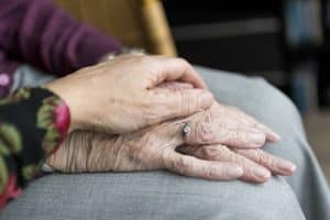 Close up of a person’s hand cradling the hands of a senior nursing patient