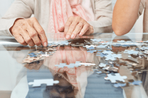 An elderly woman working on a puzzle atop a glossy table 