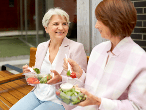 Two older women sitting outside eating salad