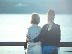 A blonde woman standing with her arm around her mother looking out over a body of water
